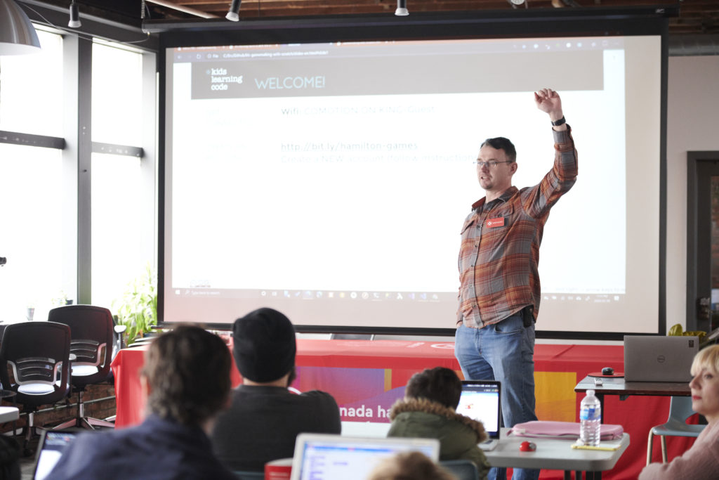 Instructor standing in front of class with a raised hand