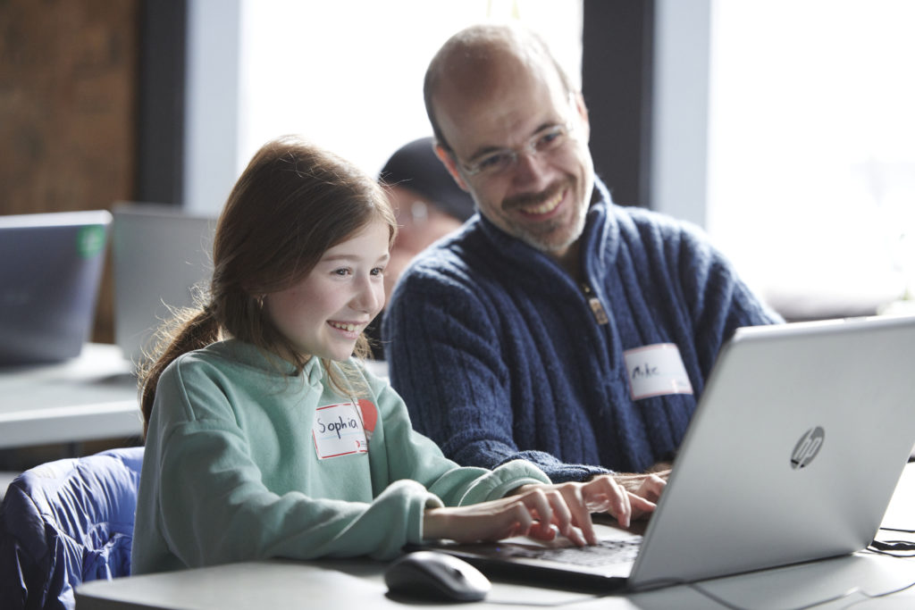 Young girl typing on the computer, she is excited, her dad is sitting with her and looking at the screen 