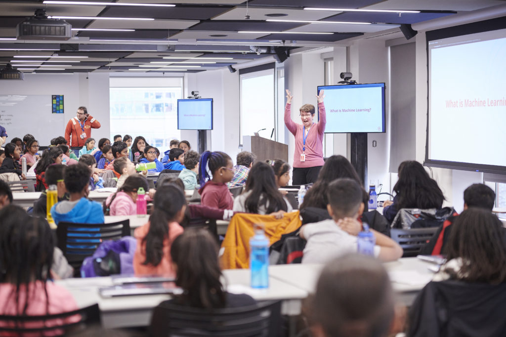 Teacher standing in front of class with hands raised