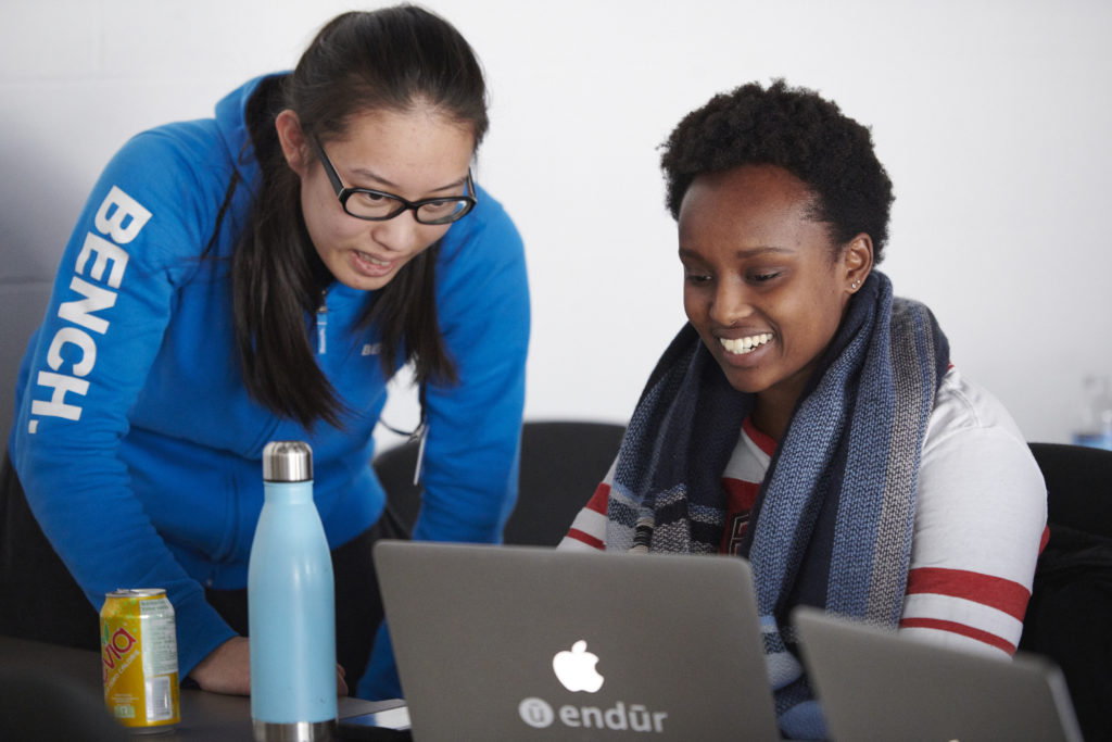 Two female learners smiling while looking at their laptop