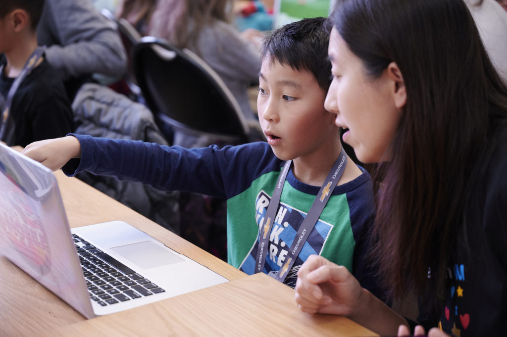 Mom and son are looking at the monitor, son is pointing something on the screen 