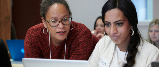 a mentor looking at a laptop of a student, who is very intently looking at her screen