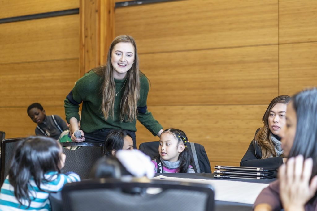 Teacher smiling, leaning over to hear what student is saying